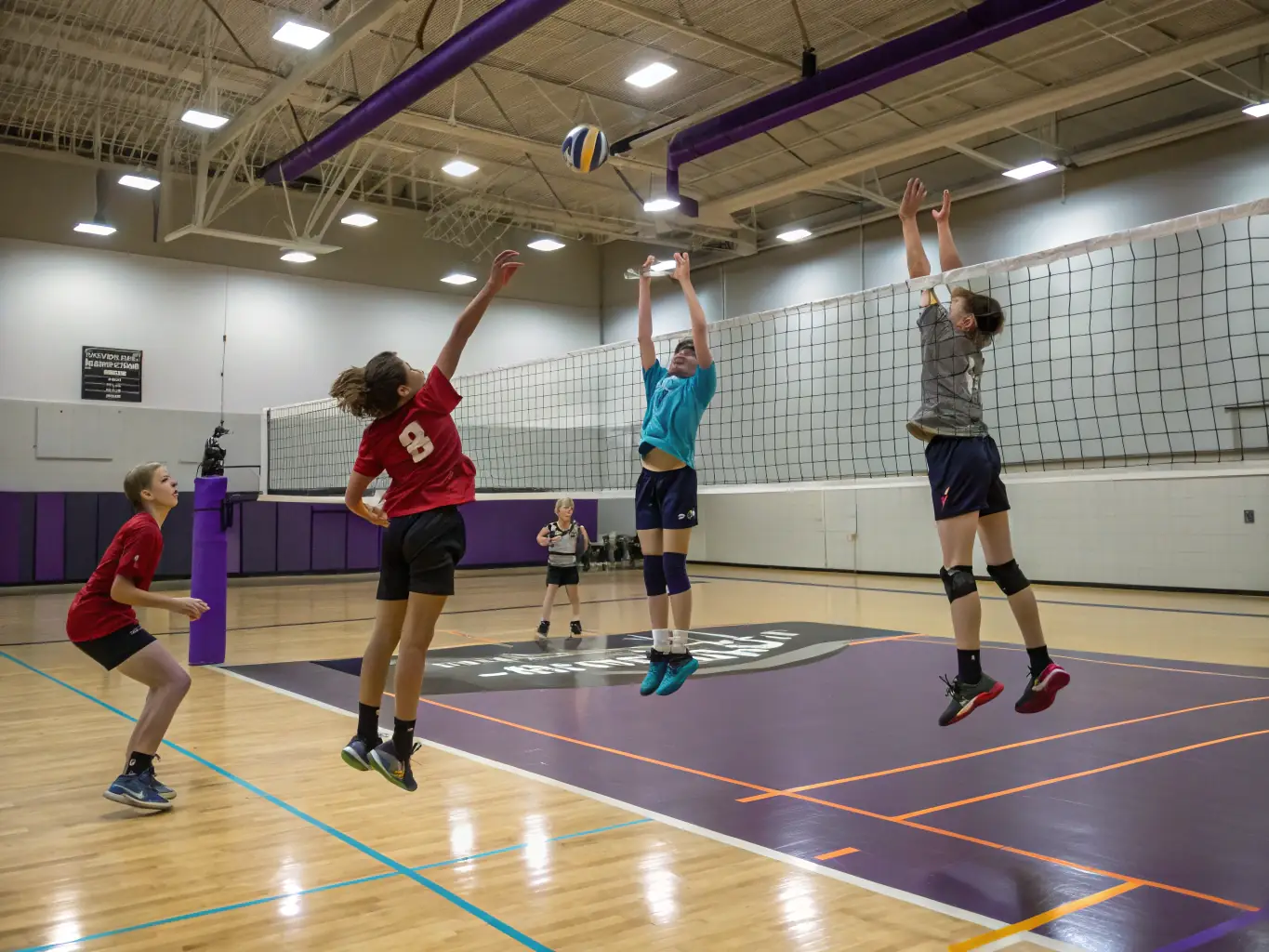 A dynamic action shot of young volleyball players in a training session, focusing on teamwork and skill development, set against the backdrop of a well-lit indoor sports hall.